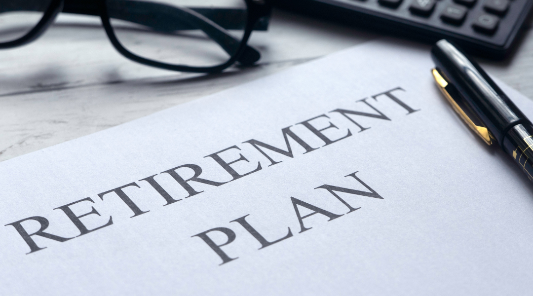 Piece of paper on desk that says "Retirement Plan" on it next to glasses, a pen, and a calculator.
