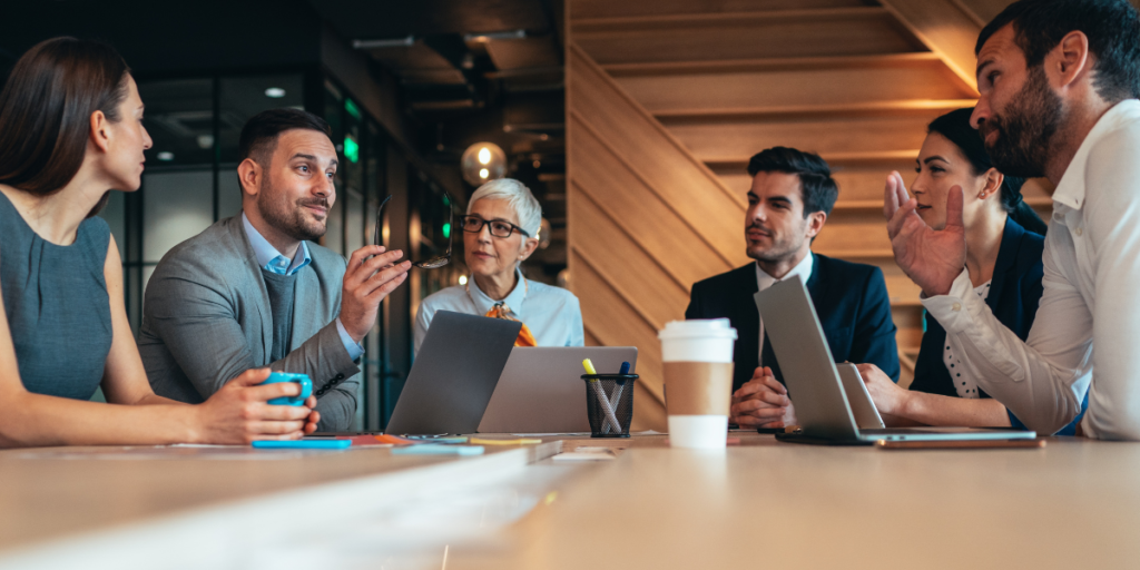 Businessmen and women who share fiduciary duty for a company speaking around a conference table. 