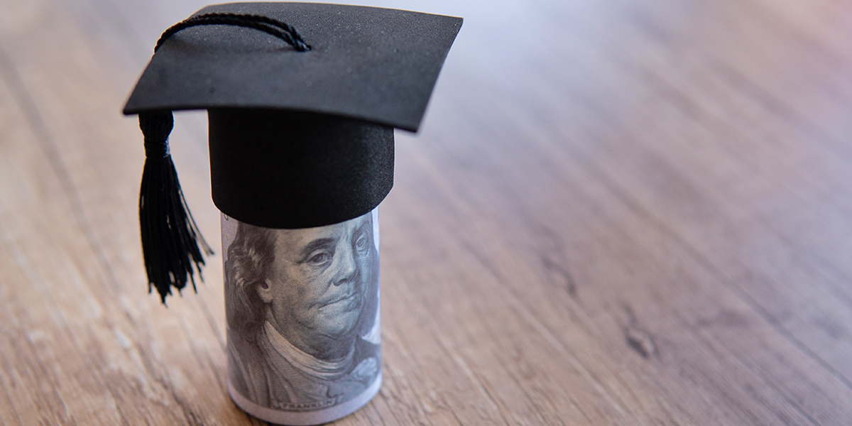 Closeup image of graduation cap and money on table.