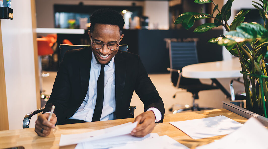 smiling man sitting at desk looking at paperwork