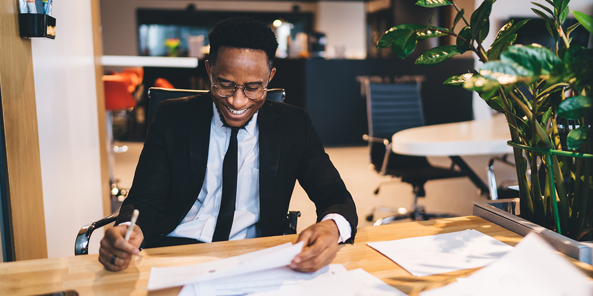 smiling man sitting at desk looking at paperwork